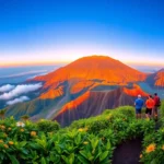 Hikers overlooking Mount Rinjani at sunrise from the crater rim, surrounded by lush greenery and volcanic landscape.